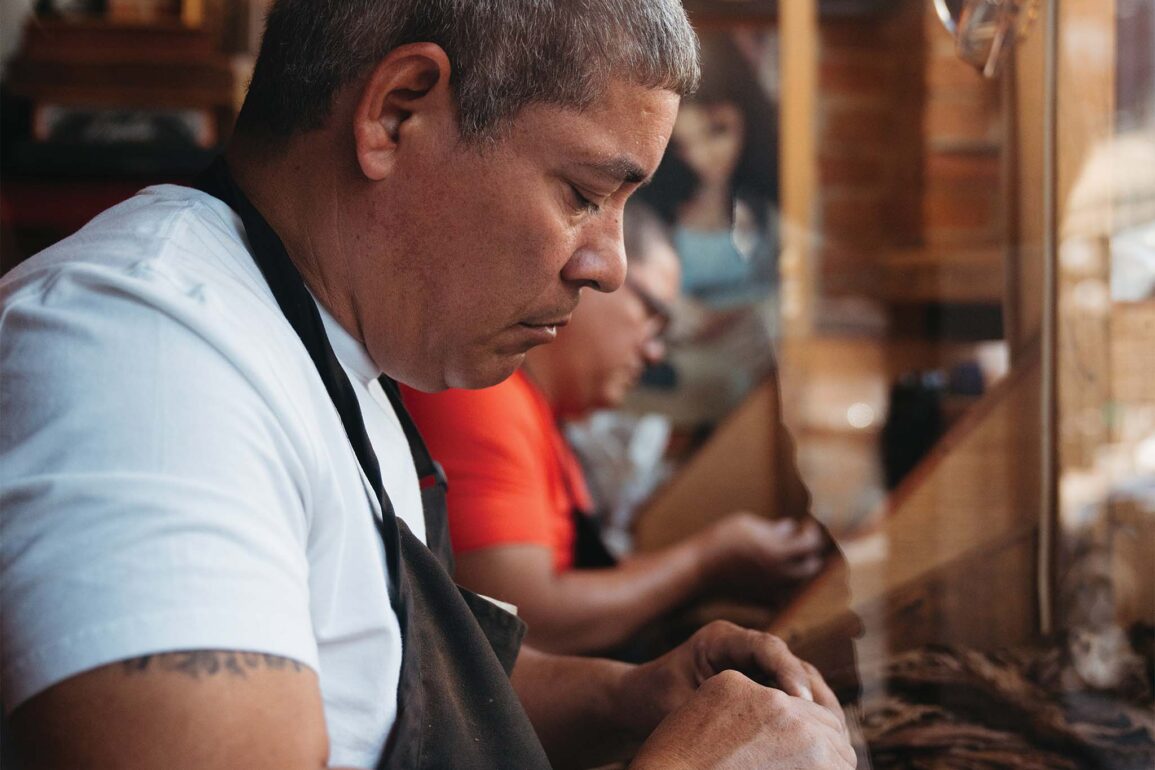 a person in an apron looking at a piece of paper - making a cigar