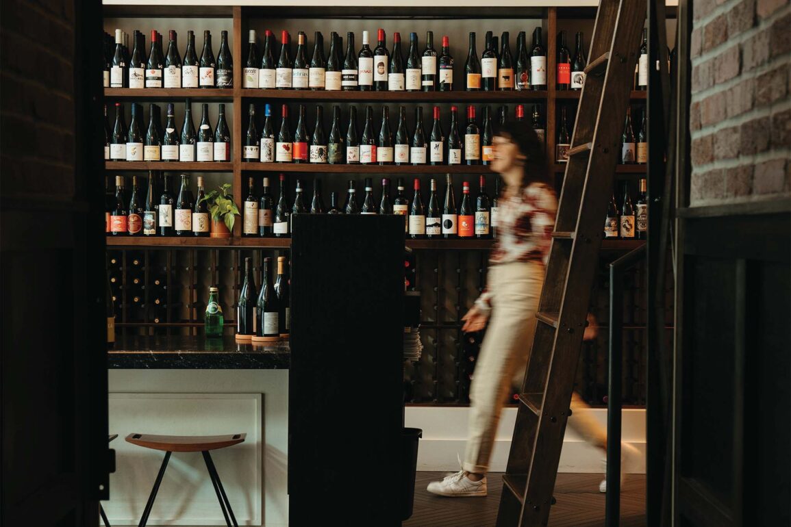a person walking in front of a shelf of wine bottles