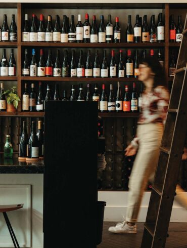 a person walking in front of a shelf of wine bottles